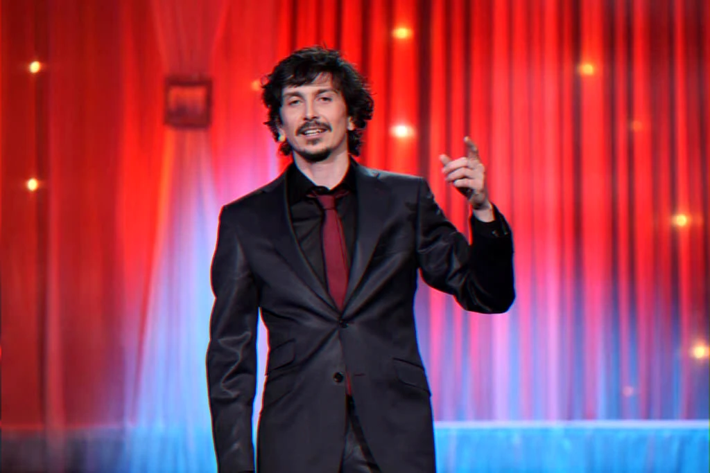 Comedian on stage announces shift to collaborative trio and theatre formats